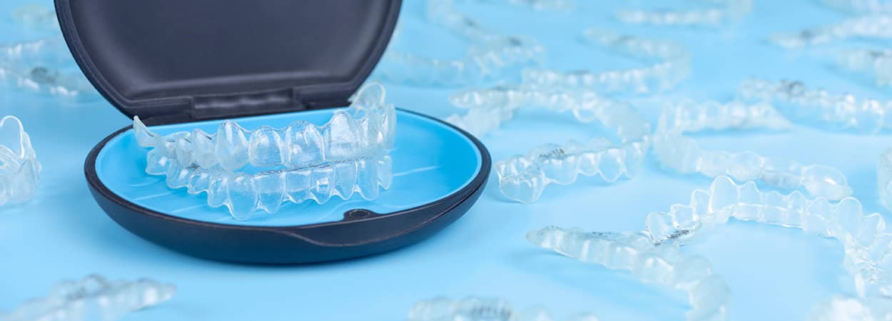 Aligneurs transparents en plastique dans un étuis et répandus sur une surface bleue