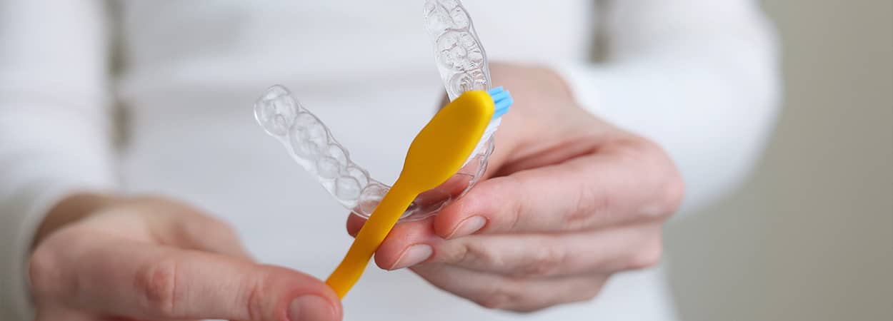 Une brosse à dent frotte un aligneur dentaire transparent