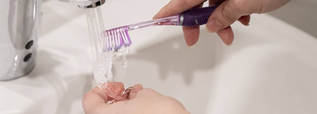 Aligneur dentaire se faisant nettoyer sous l'eau du robinet à l'aide d'une brosse à dent